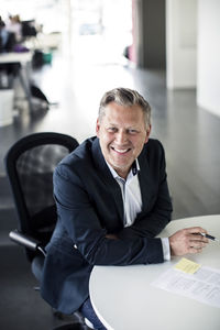 High angle portrait of happy mature businessman sitting at desk in office