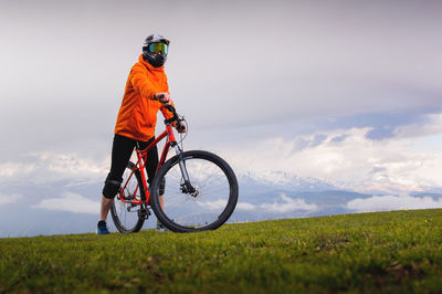 Portrait of a young cyclist standing against the backdrop of a summer landscape with a mountain in