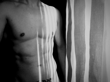 Close-up of shirtless man standing against black background