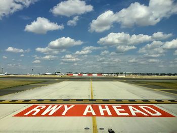 Road sign on airport runway against sky