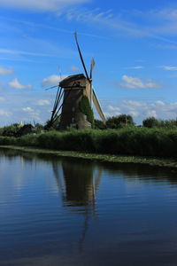 Traditional windmill by lake against sky