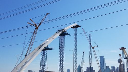 Low angle view of cranes against clear blue sky