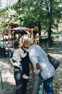 Father kissing daughter while mother carrying her at park