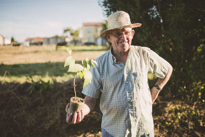 Portrait of smiling farmer with straw hat holding a plant in his hands