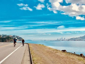 Rear view of people riding bicycle at beach against sky