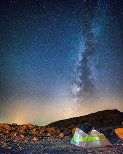 Tent by mountain against star field at night