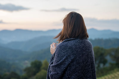 Rear view of woman standing on mountain against sky