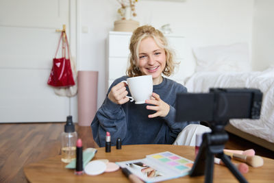 Portrait of young woman using mobile phone while sitting on bed at home