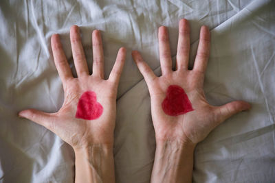 Cropped hands of woman with heart shape drawing on bed