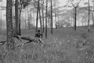 Man sitting on field by trees in forest