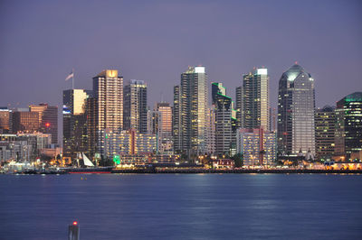 Illuminated cityscape by sea against sky at night