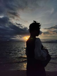 Silhouette woman standing at beach against sky during sunset