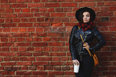 Portrait of young woman standing against brick wall