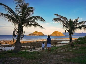 Rear view of mother and son looking at sea while standing against sky