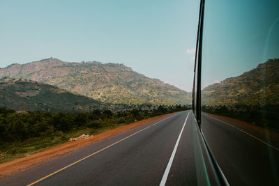 View of country road by mountains and a bus window against sky