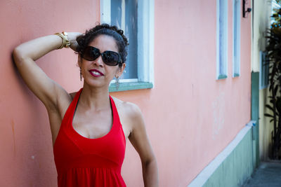 Portrait of young woman wearing sunglasses standing against wall