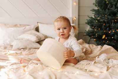 Funny funny little girl baby opens christmas gift box sitting on bed at home on holiday