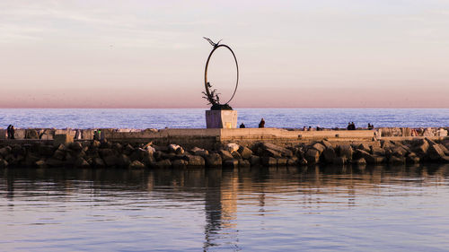 Sculpture on walkway amidst sea at sunset