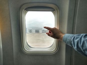 Cropped hand of man pointing towards window in airplane