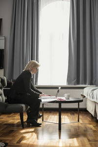Side view of mature businesswoman using laptop by window at hotel room