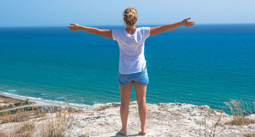 Rear view of woman standing on cliff against sea