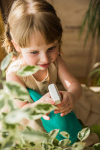 High angle view of girl spraying water on plants at home