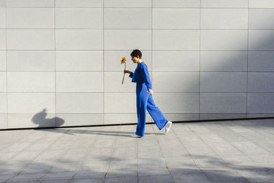 Woman with sunflower walking in front of wall on sunny day