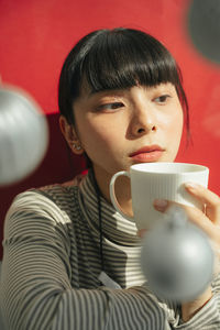 Portrait of young woman holding coffee cup against red wall