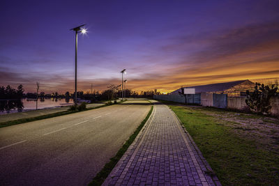 Street lights on road against sky at sunset
