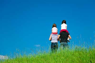 Rear view of mother and daughter walking on field against clear blue sky