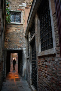 Rear view of woman walking in alley amidst buildings