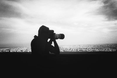 Silhouette man photographing camera on beach against sky