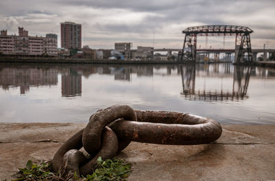 Metallic bridge over river against sky in city