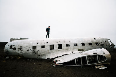 Young man standing on broken airplane on field against clear sky