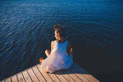 Rear view of young woman sitting on pier over lake during sunset