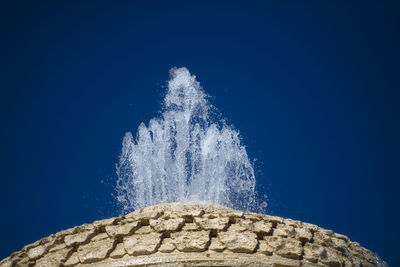 Low angle view of water splashing on rocks against blue sky