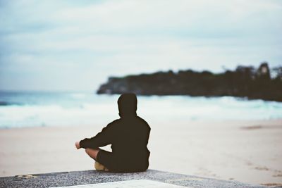 Man sitting at beach against sky