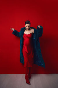 Portrait of a beautiful pregnant woman in a fur coat stands on a green background