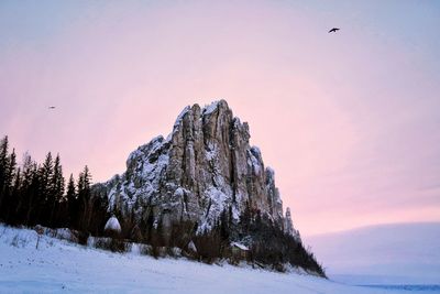 Low angle view of rock on snow covered landscape against sky at sunset