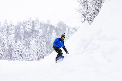 Male snowboarder in warm clothes, goggles and action camera on helmet riding along snowy road in winter woods in mountains