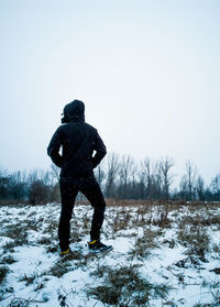 Rear view of young man standing on snow covered field against sky