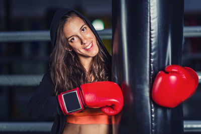 Portrait of female boxer smiling while standing with punching bag in gym