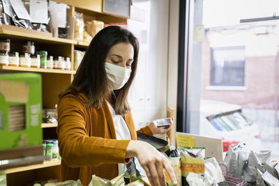 Young woman choosing food in grocery store during covid-19