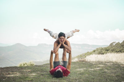 Couple doing acroyoga on mountain in front of sky