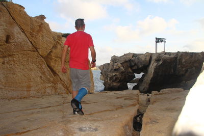 Rear view of mature man walking on rock formation against sky