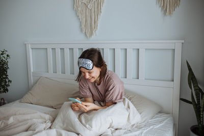 Side view of young woman sitting on bed at home