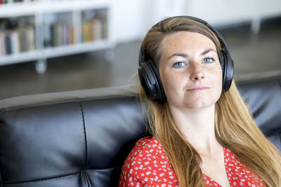 Portrait of young woman listening to music through headphones while sitting on sofa at home
