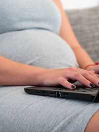 Midsection of woman using laptop while sitting on sofa at home
