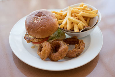 Close-up of chicken burger and french fries and onion rings in plate on table