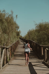 Rear view of girl running on boardwalk against clear sky